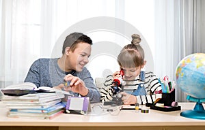 Children at home do biology lessons. The girl looks at the microscope. Home education, distance learning, home lessons