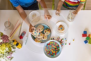Funny male brothers eat cookies with round multi-colored sweets m&m and drink milk. Top view.