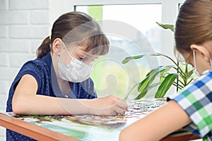 Children at home in protective masks play board puzzles