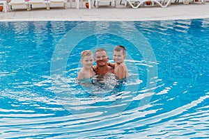 Children hugging his father`s neck in the blue pool