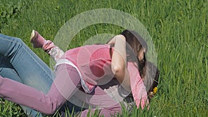 Children are hugging mom in the park. The girls drop mother on the green grass. Family in the park on a sunny afternoon.