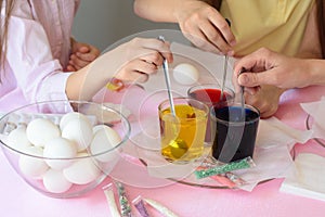 Children interfere with a solution with food coloring in glasses to paint Easter eggs
