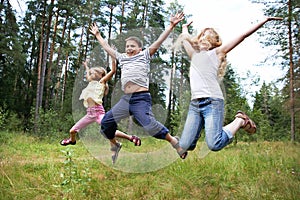 Children jump on lawn in summer forest
