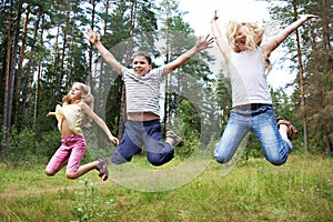 Children jump on lawn in summer forest