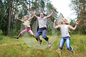 Children jump on lawn in summer forest