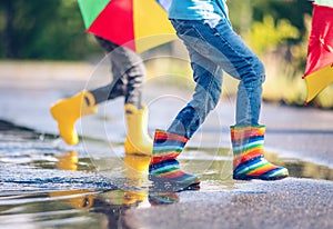 Children jumping in the puddle in rubber boots