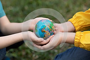 Children kid girl in a yellow raincoat and boy holding globe in a hands outdoor in park or forest. World Earth Day concept. Green