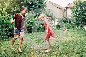 Children kids splashing with gardening hose sprinkler on backyard on summer day
