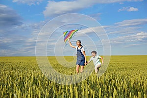 Children with a kite run across the wheat field in the summer. C