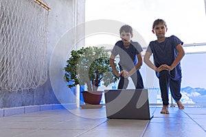 Children with laptop computer doing sport exercises at home on balcony. Sport, healhty lifestyle, active leisure, stay