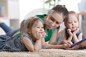 Children laughing and having fun reading stories with their mother laying on the floor at home