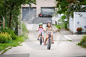 Children learning to drive a bicycle on a driveway outside.