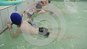 Children learning to swim in the pool. Children kick their feet in the water creating splashes of water in the