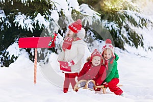 Children with letter to Santa at Christmas mail box in snow