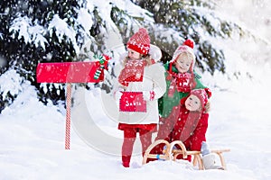 Children with letter to Santa at Christmas mail box in snow