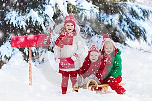 Children with letter to Santa at Christmas mail box in snow