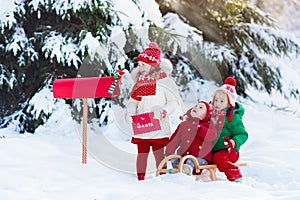 Children with letter to Santa at Christmas mail box in snow