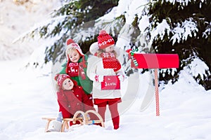 Children with letter to Santa at Christmas mail box in snow