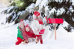 Children with letter to Santa at Christmas mail box in snow