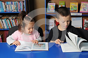 Children in library reading interesting book. Little girl and boy learning