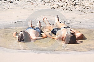 Children lie on the sand. The boys sunbathing in the water. Childhood in the puddle. Direct child