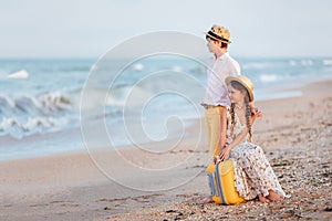 Children look in the sea.The girl and the boy are sitting on a yellow suitcase on the beach