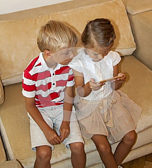 children look at the smartphone screen. the boy looks into the phone to the happy sister