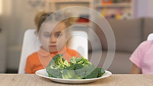 Children looking with disgust at broccoli, refusing to eat healthy vegetables