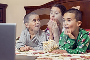 Children looking at laptop with cartoons showing before sleeping in bed. Three children in bed watching a movie on a laptop