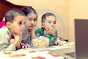 Children looking at laptop with cartoons showing before sleeping in bed. Three children in bed watching a movie on a laptop