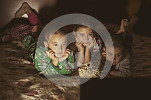 Children looking at laptop with cartoons showing before sleeping in bed. Three children in bed watching a movie on a laptop. toned