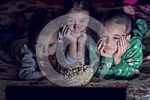 Children looking at laptop with cartoons showing before sleeping in bed. Three kids in bed watching a movie on a laptop