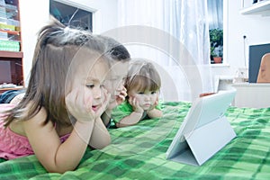 Children looking on pad lying on bed at home. Children time spending. Kids using tablet