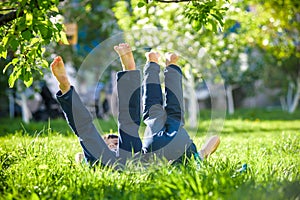 Children lying on green grass in park on a summer day with their legs lifted up to the sky