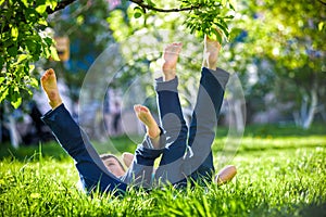 Children lying on green grass in park on a summer day with their legs lifted up to the sky