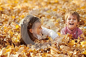 Children are lying and palying in fallen leaves in autumn city park.