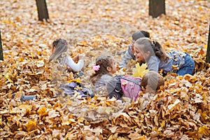 Children are lying and playing on fallen leaves in autumn city park.