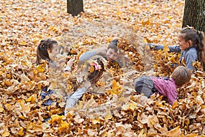 Children are lying and playing on fallen leaves in autumn city park.