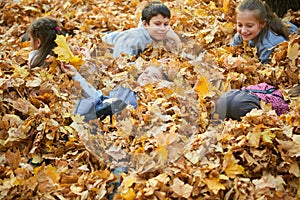 Children are lying and playing on fallen leaves in autumn city park.