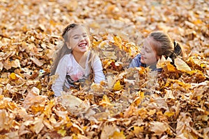 Children are lying and playing on fallen leaves in autumn city park.