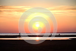 Children and a man riding a bike on the beach at sunset