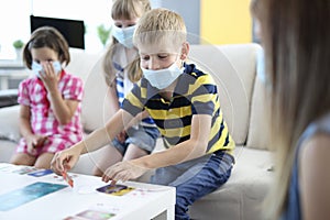 Children in medical protective masks play board games at home.