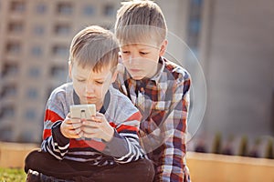 Children with mobile phone outdoor. Boys smiling, looking to phone, playing games or using application