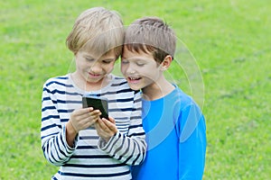 Children with mobile phone outdoor. Two boys smiling, looking to screen, playing games or using application. Technology