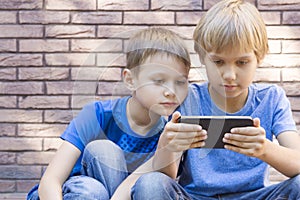 Children with mobile phone. Two boys looking at screen, playing games or using application. Outdoor. Technology
