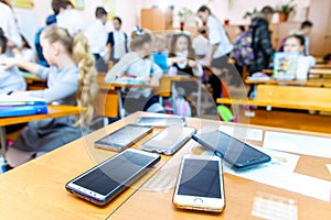 Children mobile phones stand on a teacher`s desk in a school class