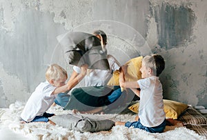 Children with mom on the bed have fun and fight pillows.