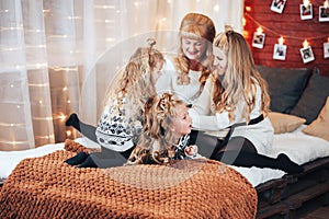 Children with mom and grandmother are sitting hugging on a large bed. Christmas mood. Against the background of a brick wall with