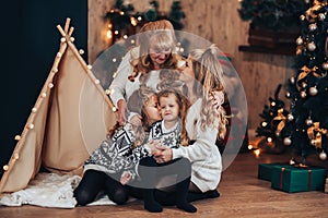 Children with mom and grandmother are sitting hugging on a large bed. Christmas mood. Against the background of a brick wall with