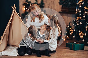 Children with mom and grandmother are sitting hugging on a large bed. Christmas mood. Against the background of a brick wall with